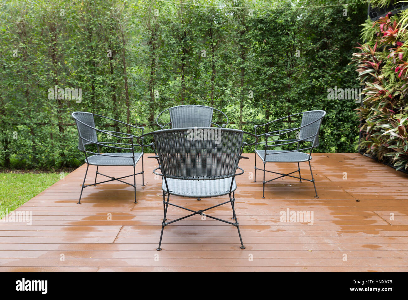 rattan wicker chair and desk on patio beside garden in rainy day Stock