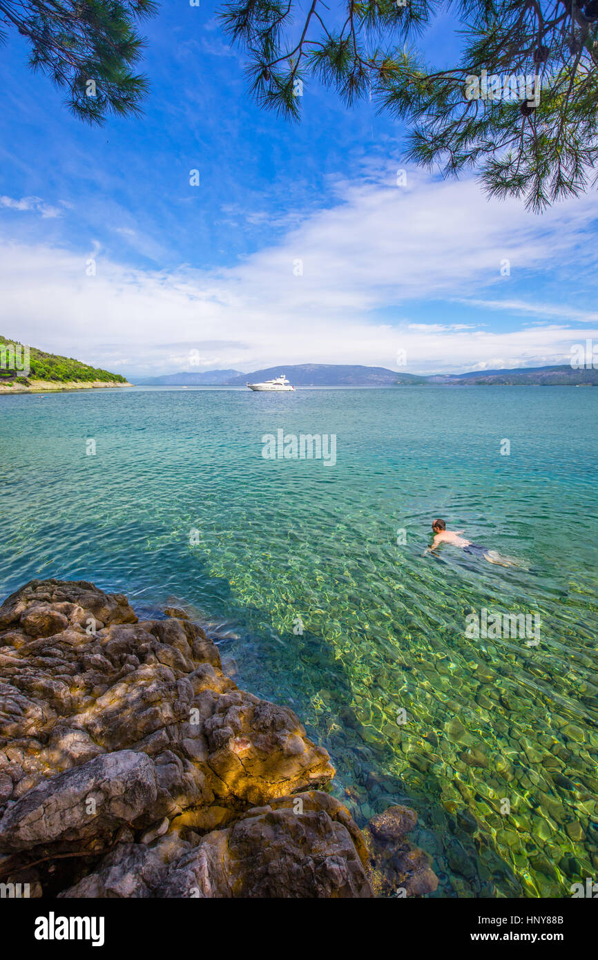 Young man swimming in stone beach with crystal clear tourquise sea in island Cres in Croatia Stock Photo