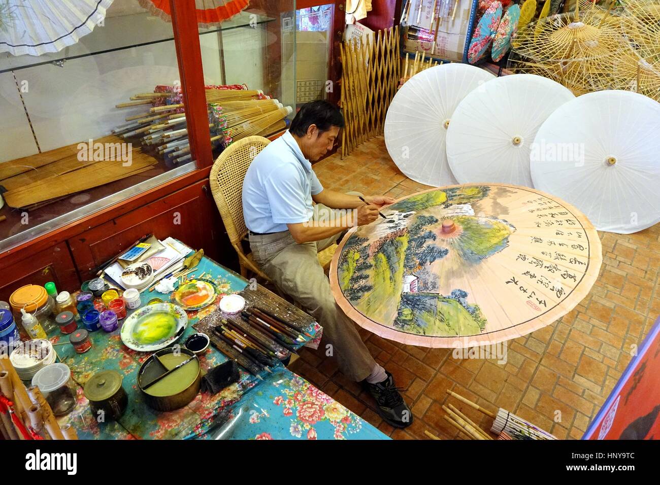 KAOHSIUNG, TAIWAN -- JULY 24, 2016: A male artist paints oil-paper umbrellas, which is a traditional art and craft product by the Chinese Hakka people Stock Photo