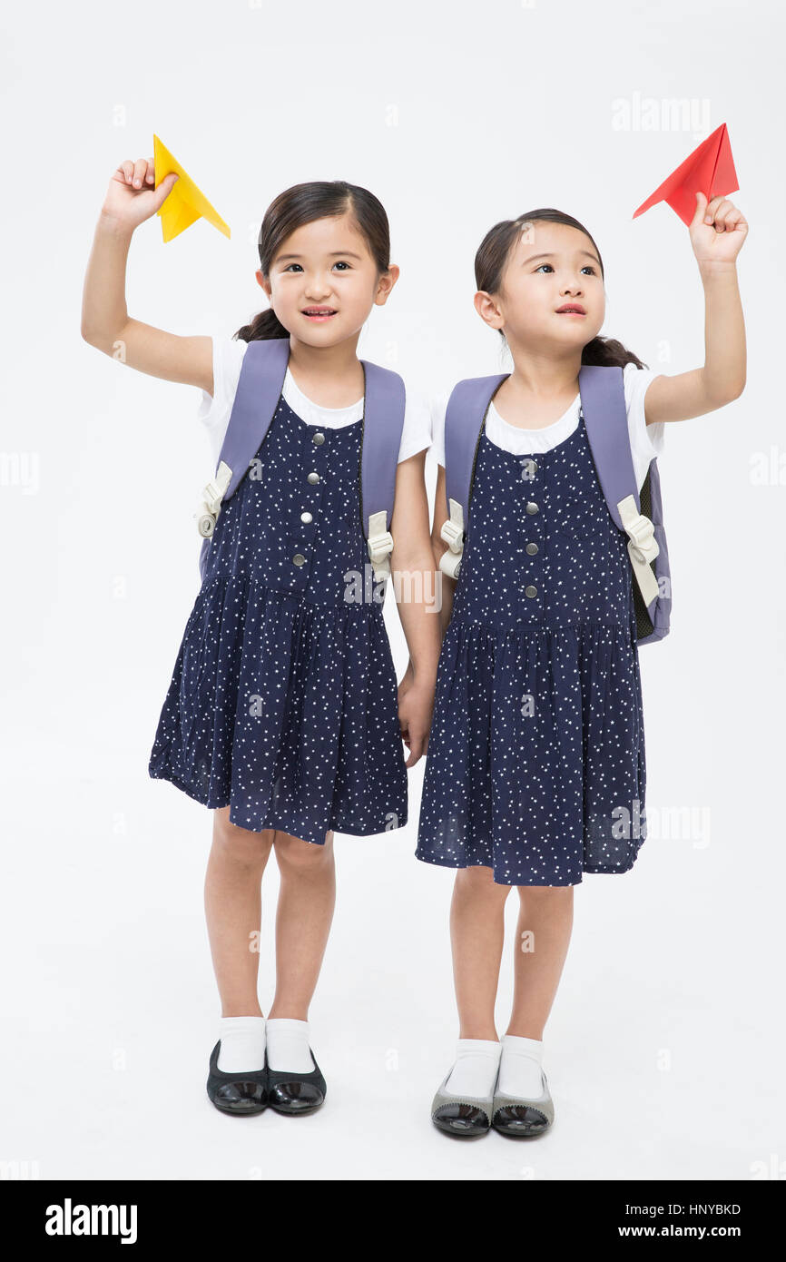 Twin girls with backpacks flying paper airplanes Stock Photo