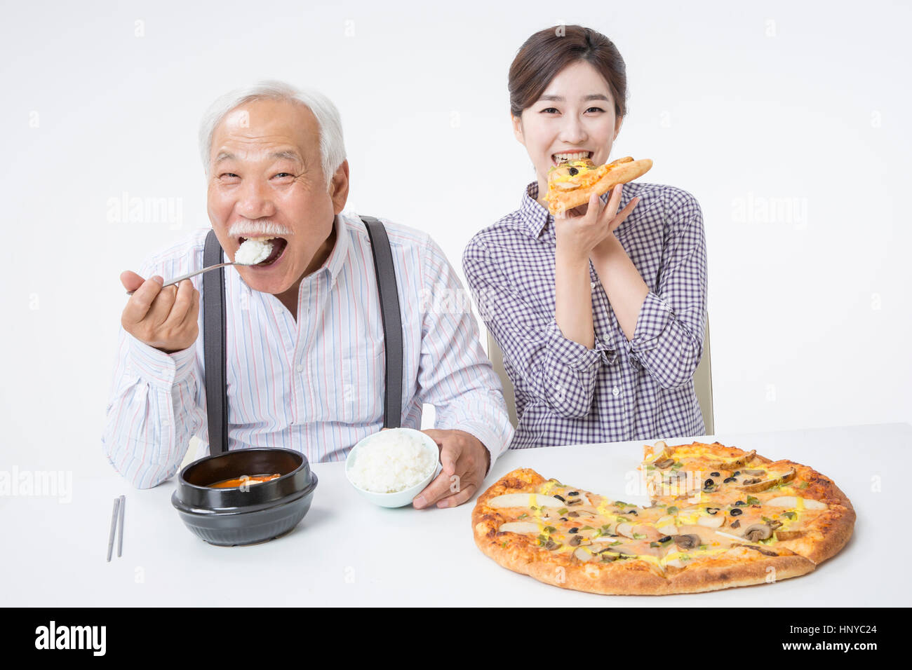 Smiling senior man eating rice and smiling young woman eating pizza Stock Photo