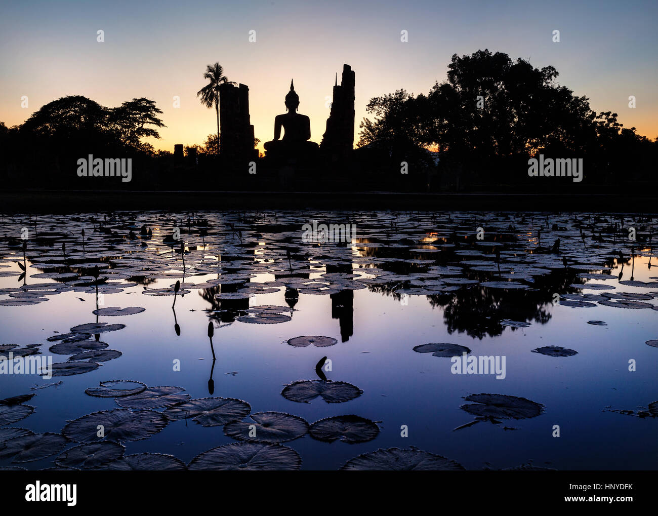 Beautiful scenery of Wat Mahathat Temple in Sukhothai Historical Park with Buddha statue silhouette and reflections on the pond in Thailand Stock Photo