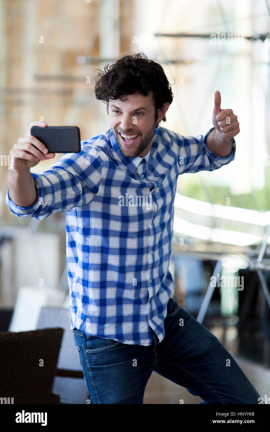 Man giving a thumbs up whiile taking a selfie with his smartphone Stock Photo
