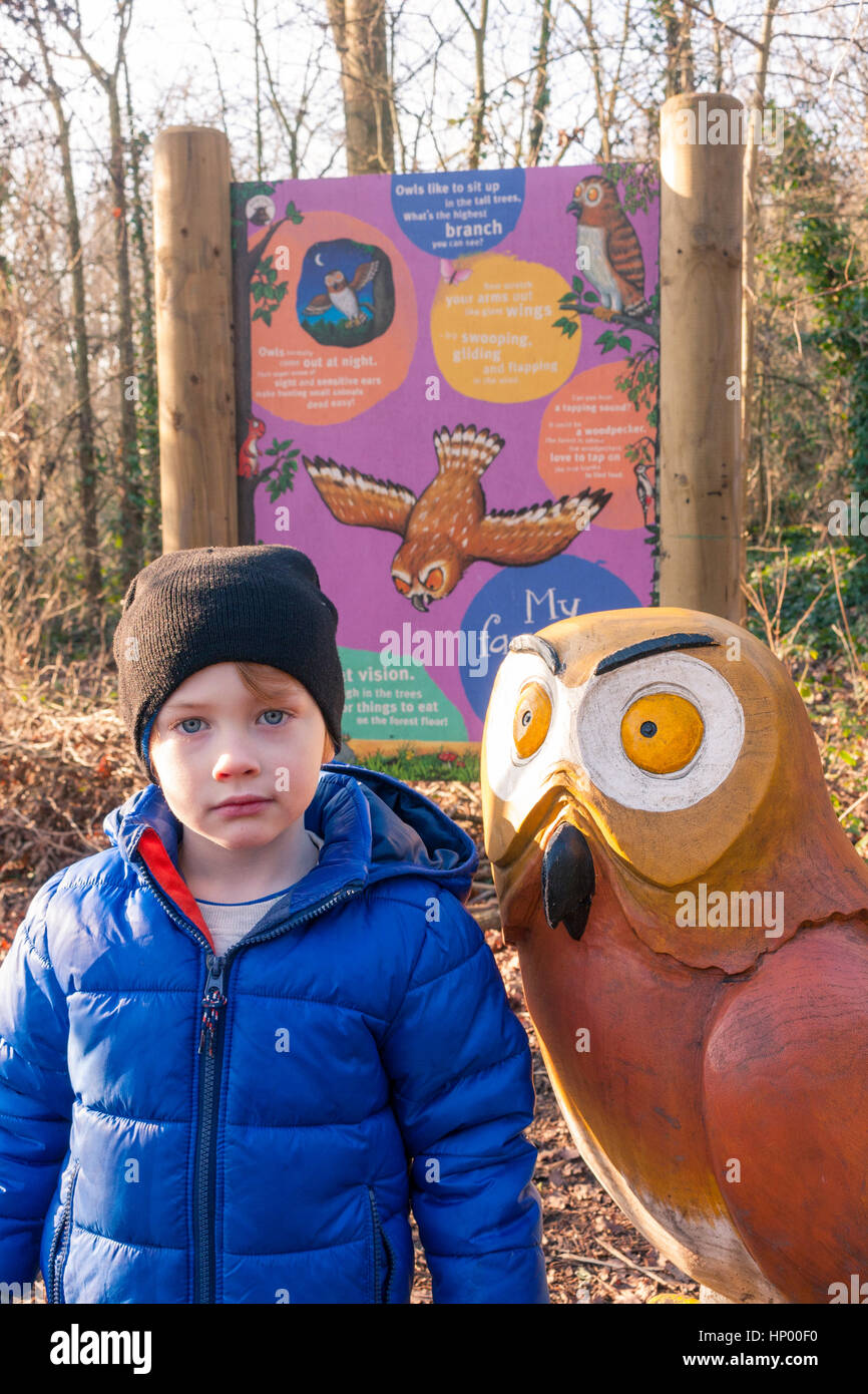 A young boy standing next to a wooden sculpture of 'Owl' (character from The Gruffalo) on the Gruffalo Trail, Horsenden Hill, Greenford, UK Stock Photo