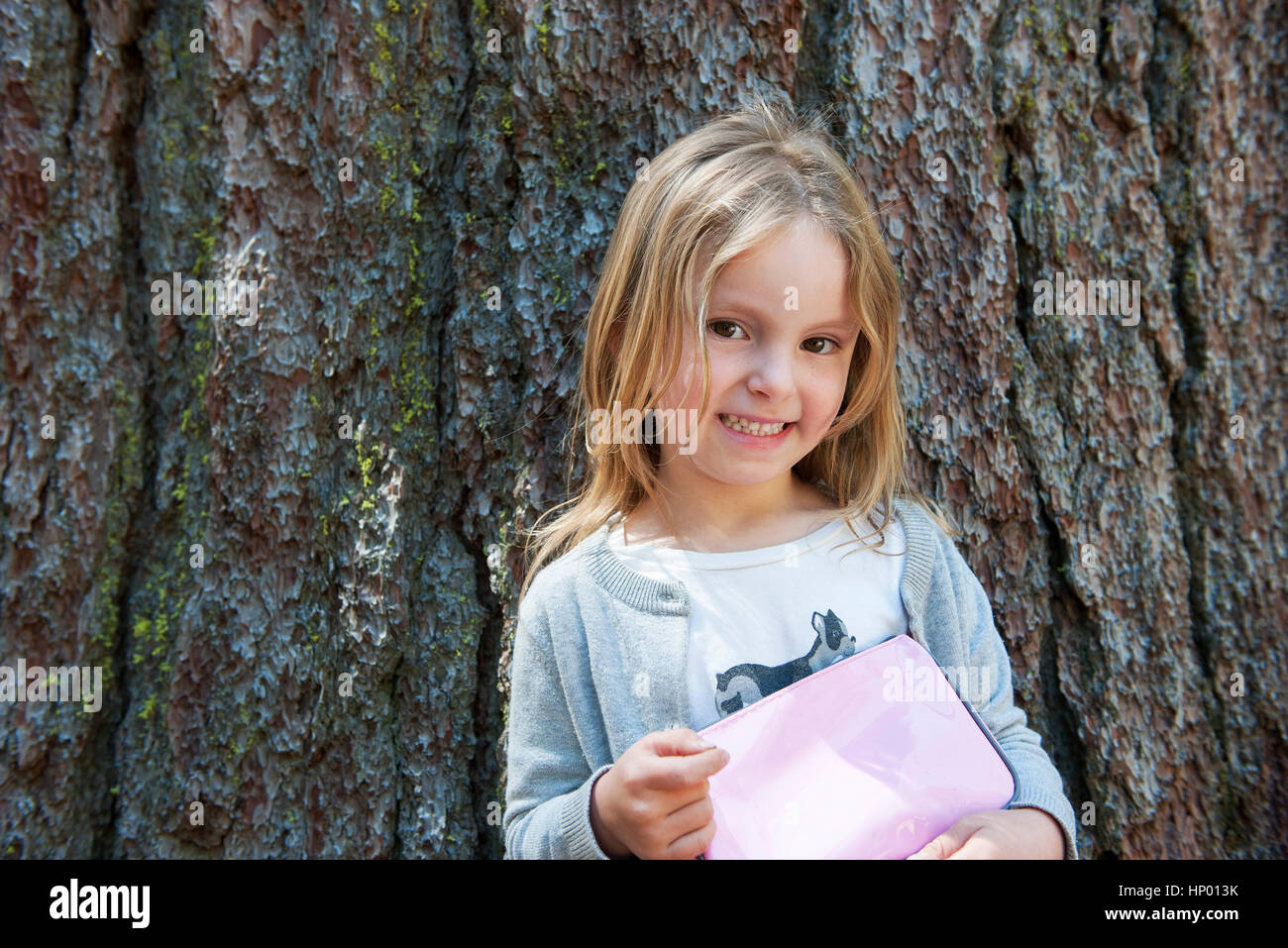 Girl leaning against tree trunk, smiling cheerfully Stock Photo