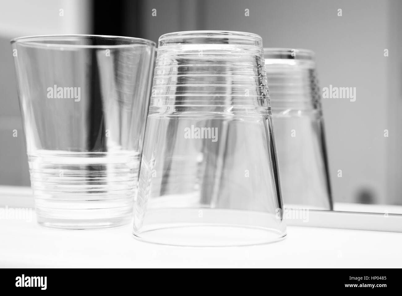 Empty glasses stand on white shelf near the mirror, black and white closeup photo Stock Photo