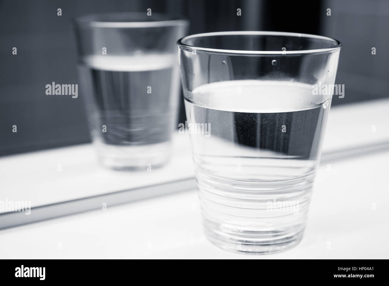 Glass of water stand on white shelf near the mirror, black and white close-up photo Stock Photo