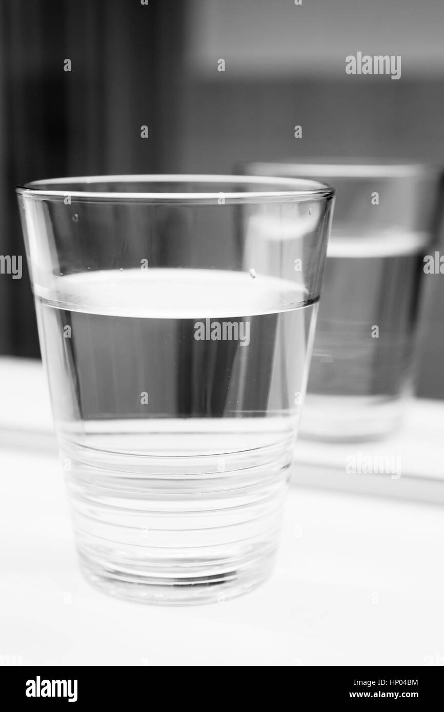 Glass of water stand on white shelf near the mirror, vertical black and white close-up photo Stock Photo