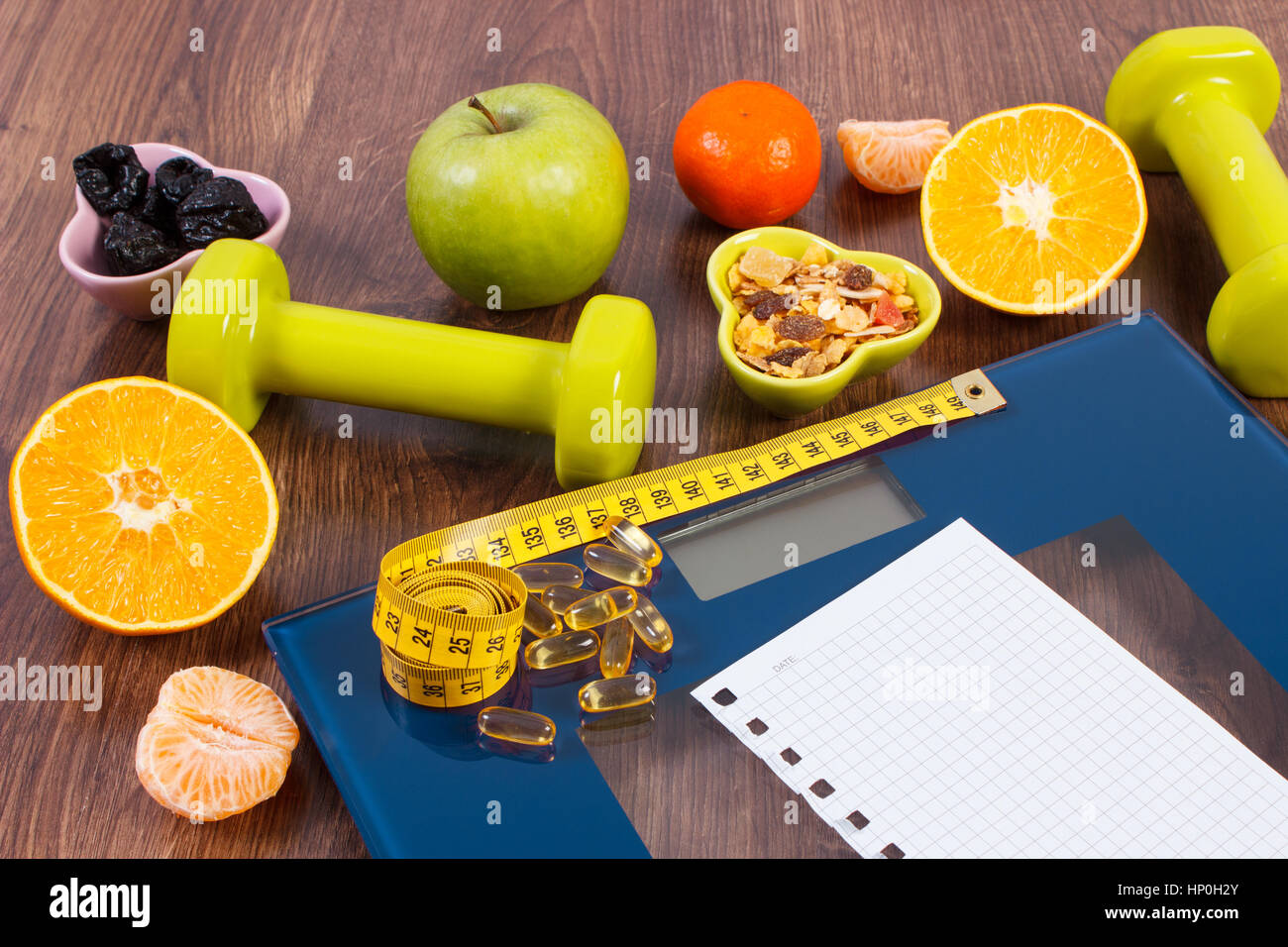 Tape measure, tablets supplements on digital bathroom scale for weight of human body, dumbbells for fitness and fresh fruits with muesli, concept of h Stock Photo