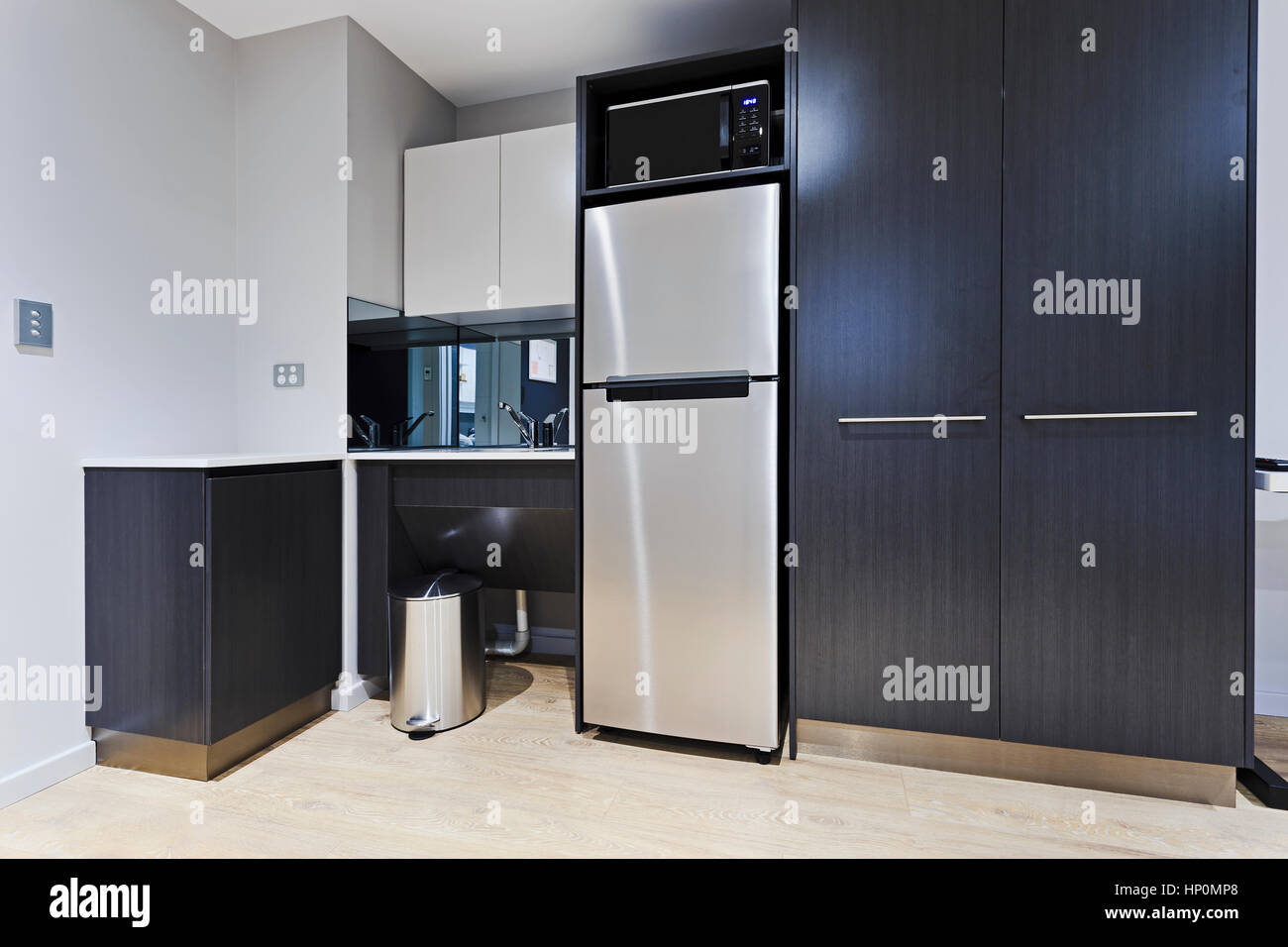 Modern stylish kitchenette corner in brand new apartment with fridge, cupboards, sink, tap and microwave oven. Stock Photo