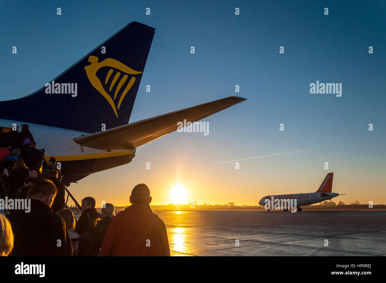 Passengers boarding a Ryanair Boeing 737-800 aircraft as an Easyjet Airbus taxis to runway at Bristol Airport, England, UK at sunrise Stock Photo