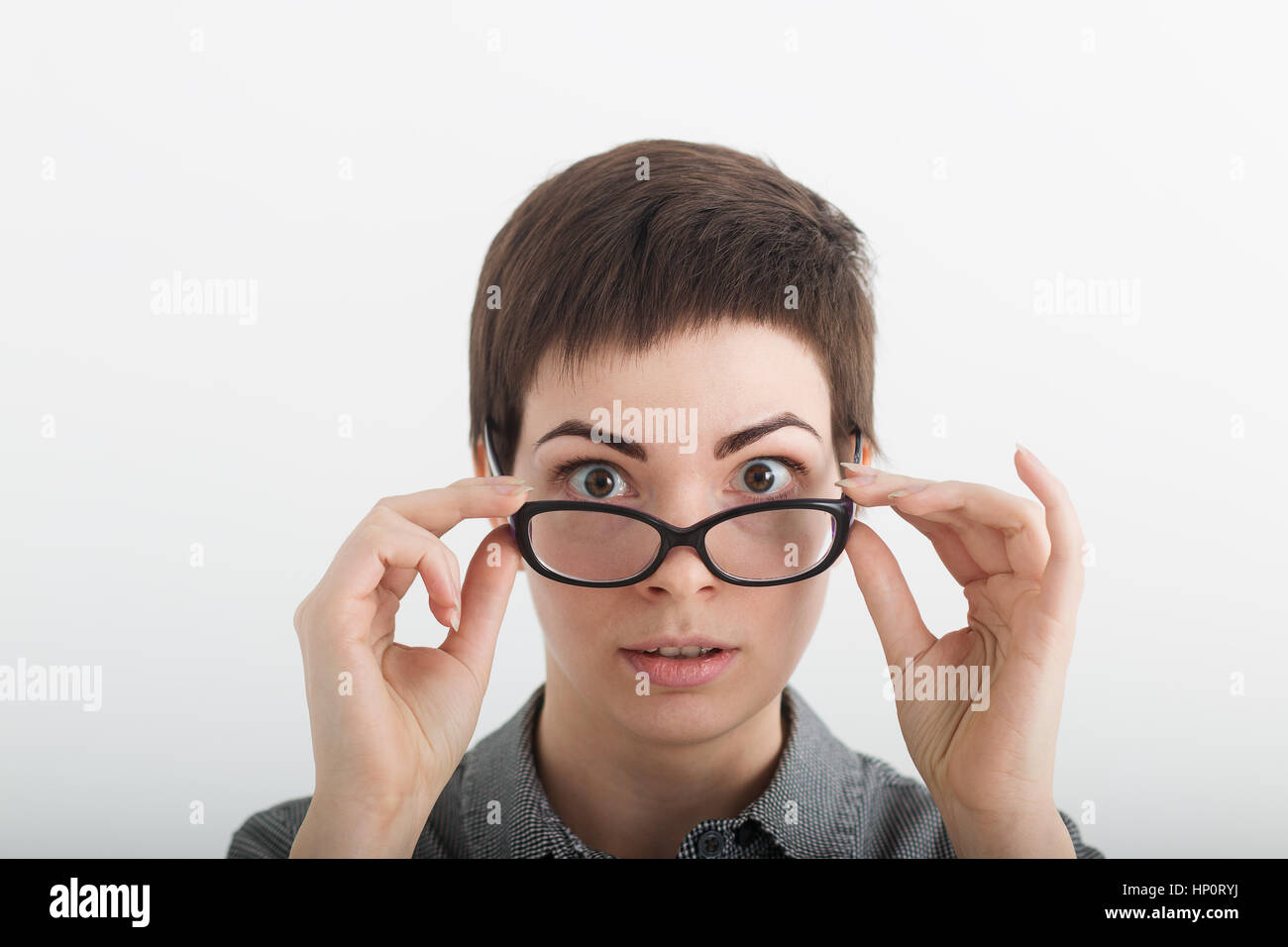 Close up of strict surprised young funny female teacher or student in glasses isolated on white background, looking over her glasses. Stock Photo