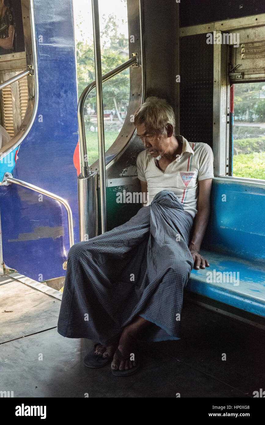 A dejected looking Burmese man in traditional clothes sits sadly on a train in Yangon Stock Photo