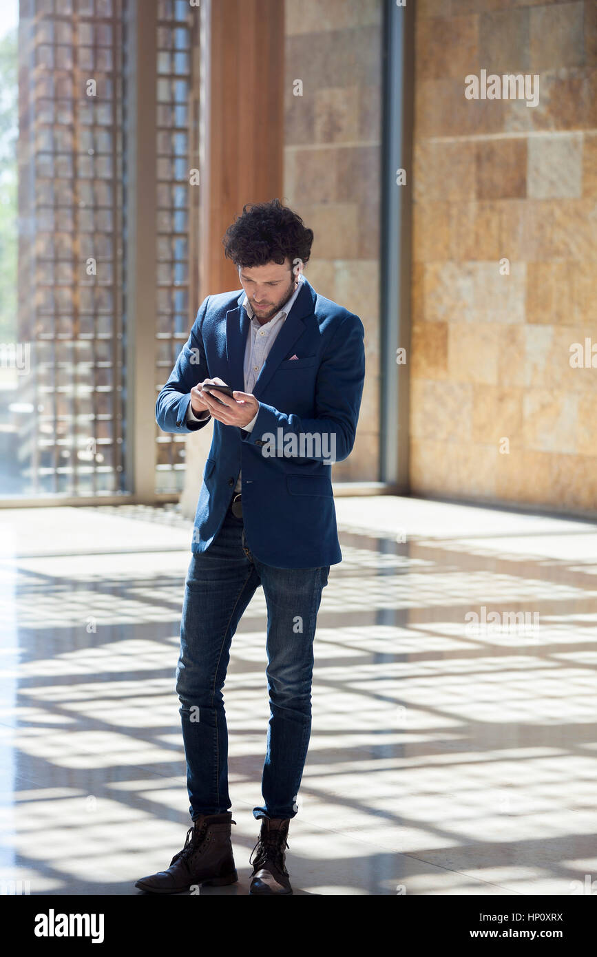 Man text messaging while walking through lobby Stock Photo