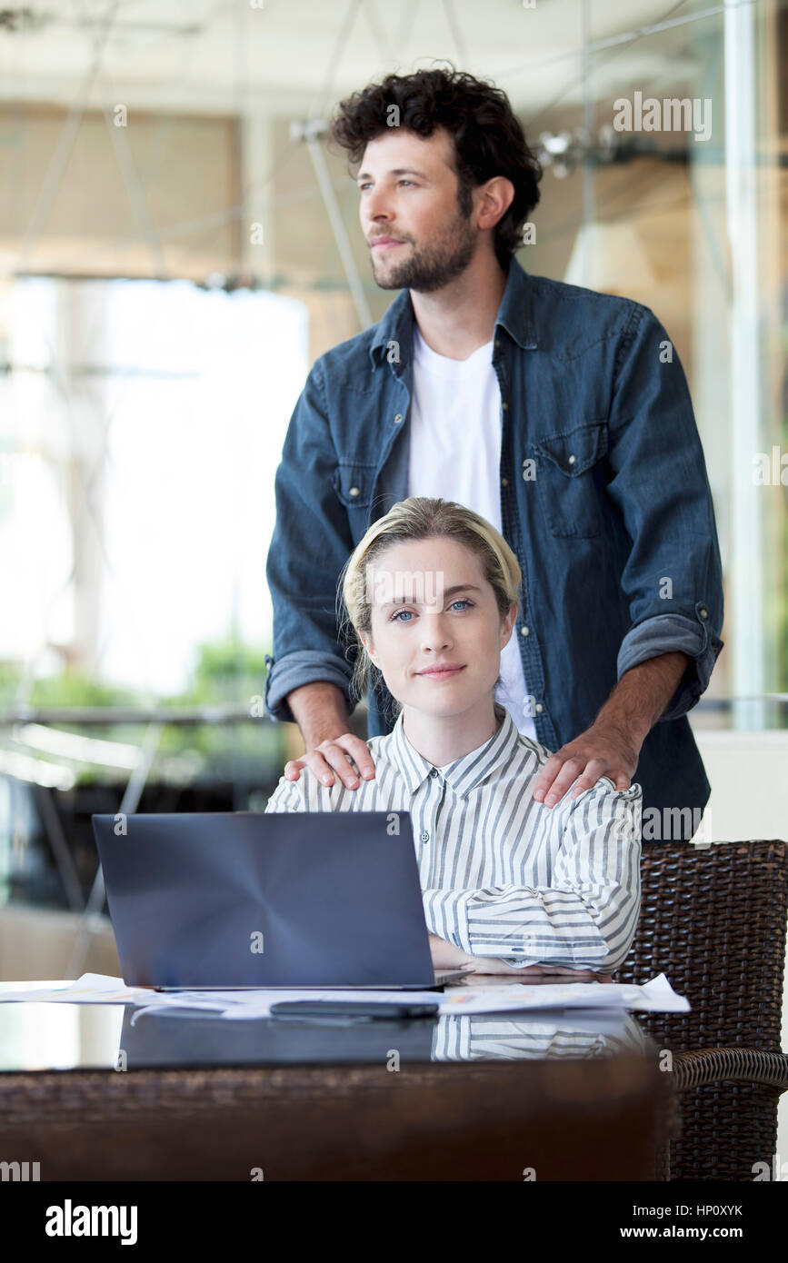 Man massaging woman's shoulders as she works on laptop computer Stock Photo