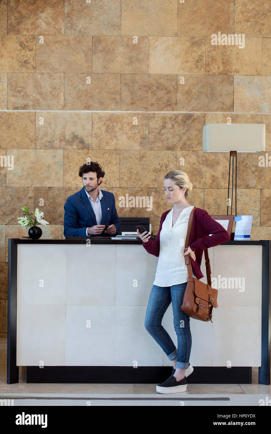 Woman looking at smartphone while waiting at reception desk Stock Photo