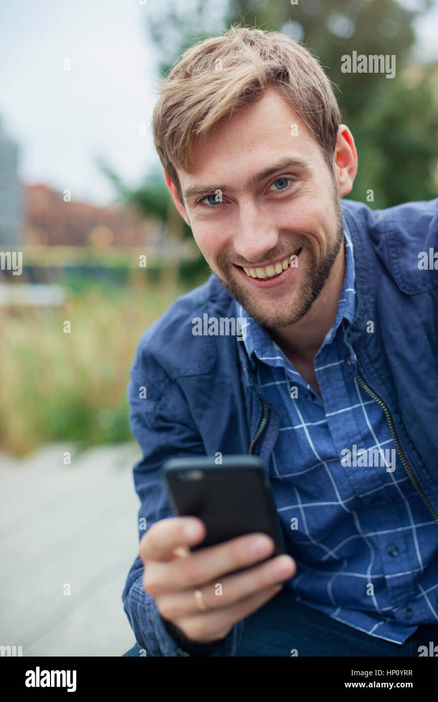 Man using smartphone outdoors, smiling, portrait Stock Photo