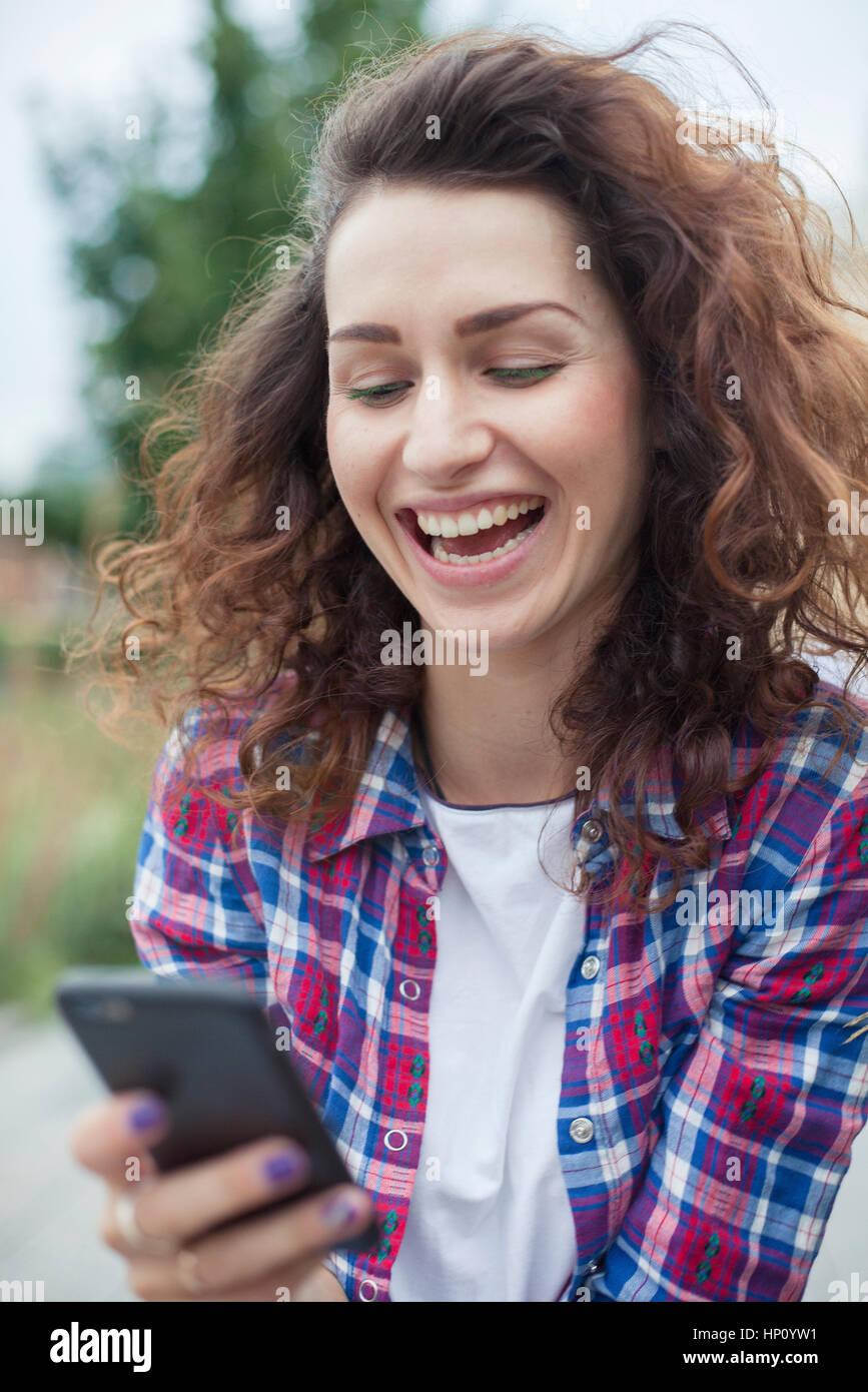 Young woman laughing while text messaging outdoors Stock Photo