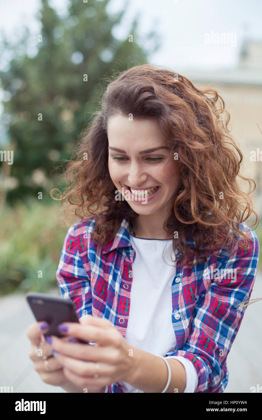 Cheerful young woman using smartphone outdoors Stock Photo