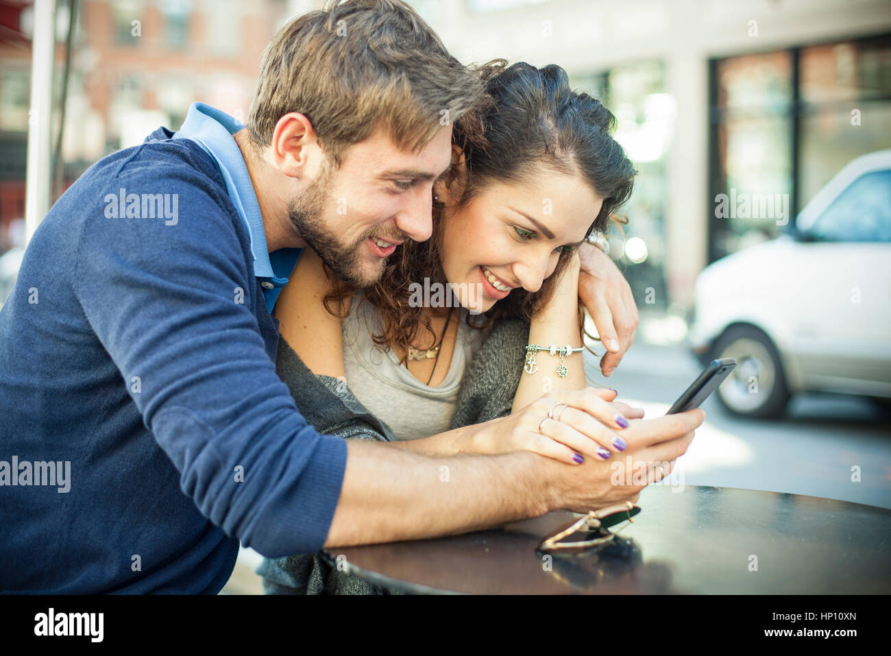 Couple sitting outdoors together, looking at smartphone Stock Photo