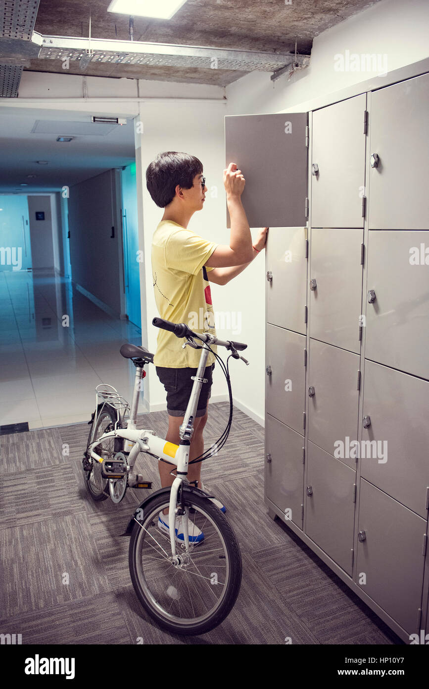 College student pausing by lockers with bicycle Stock Photo