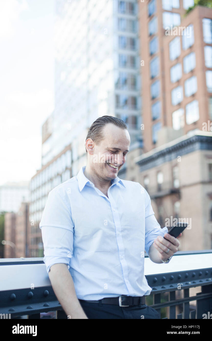 Man laughing while using smartphone outdoors Stock Photo