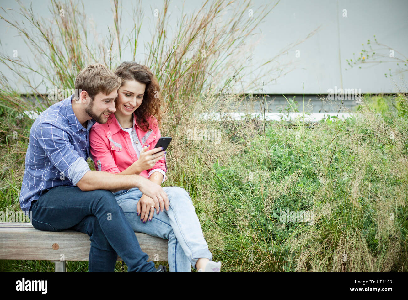 Couple sitting together on park bench, looking at smartphone Stock Photo