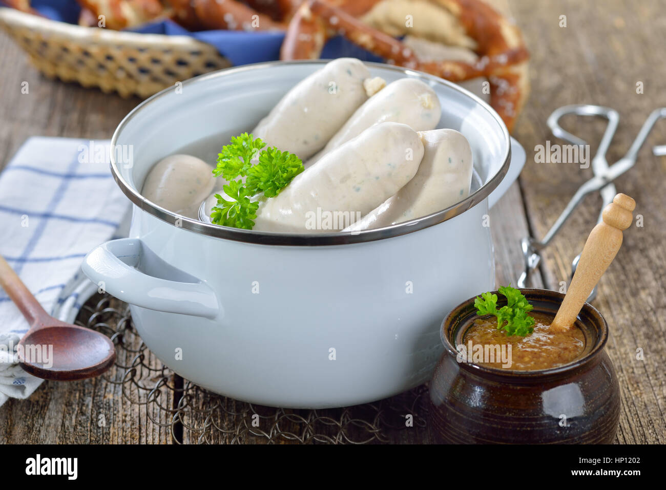 Hot Bavarian white sausages in an enamel cooking pot served on a wooden table with fresh pretzels and sweet mustard Stock Photo