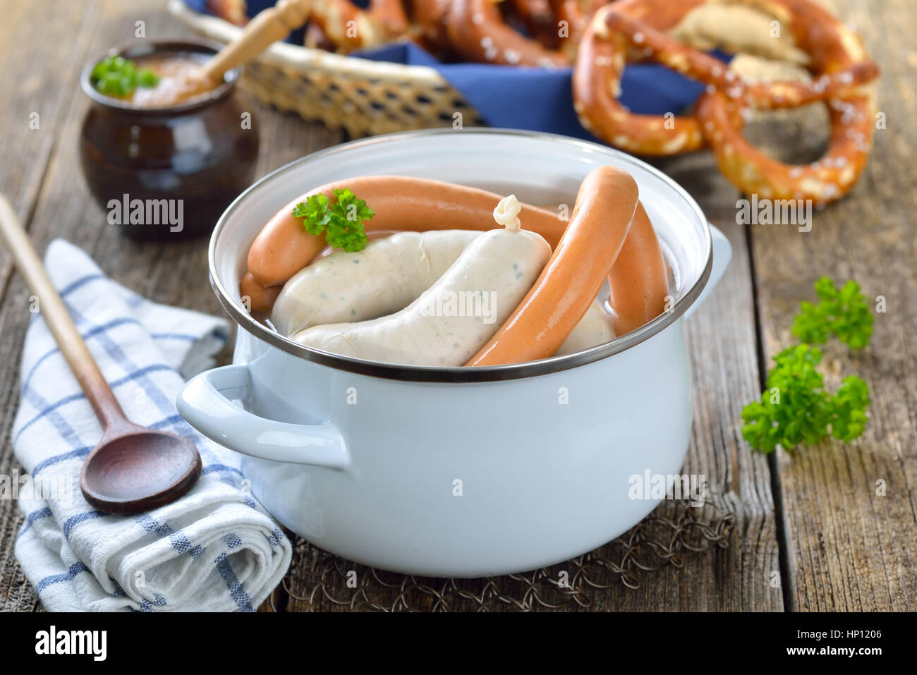 Hot Bavarian white sausages and wieners in an enamel cooking pot served on a wooden table with fresh pretzels and sweet mustard Stock Photo