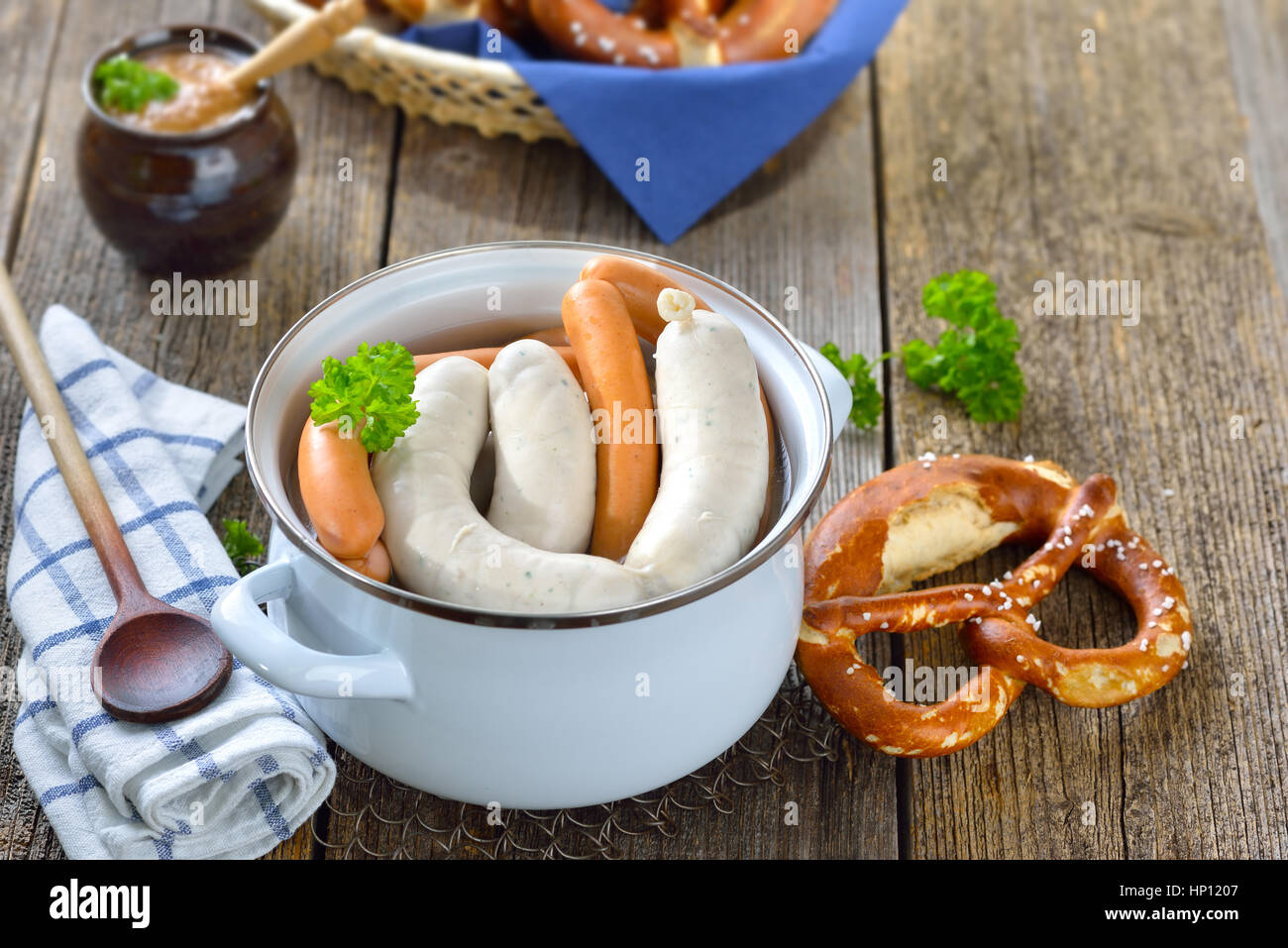 Hot Bavarian white sausages and wieners in an enamel cooking pot served on a wooden table with fresh pretzels and sweet mustard Stock Photo