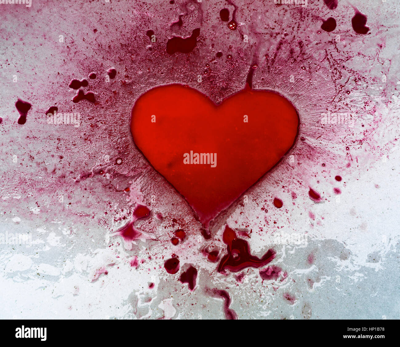 Red ink heart on ice. Red ink pooling into a heart shaped hollow, and across and into other depressions in the surface of ice. Stock Photo