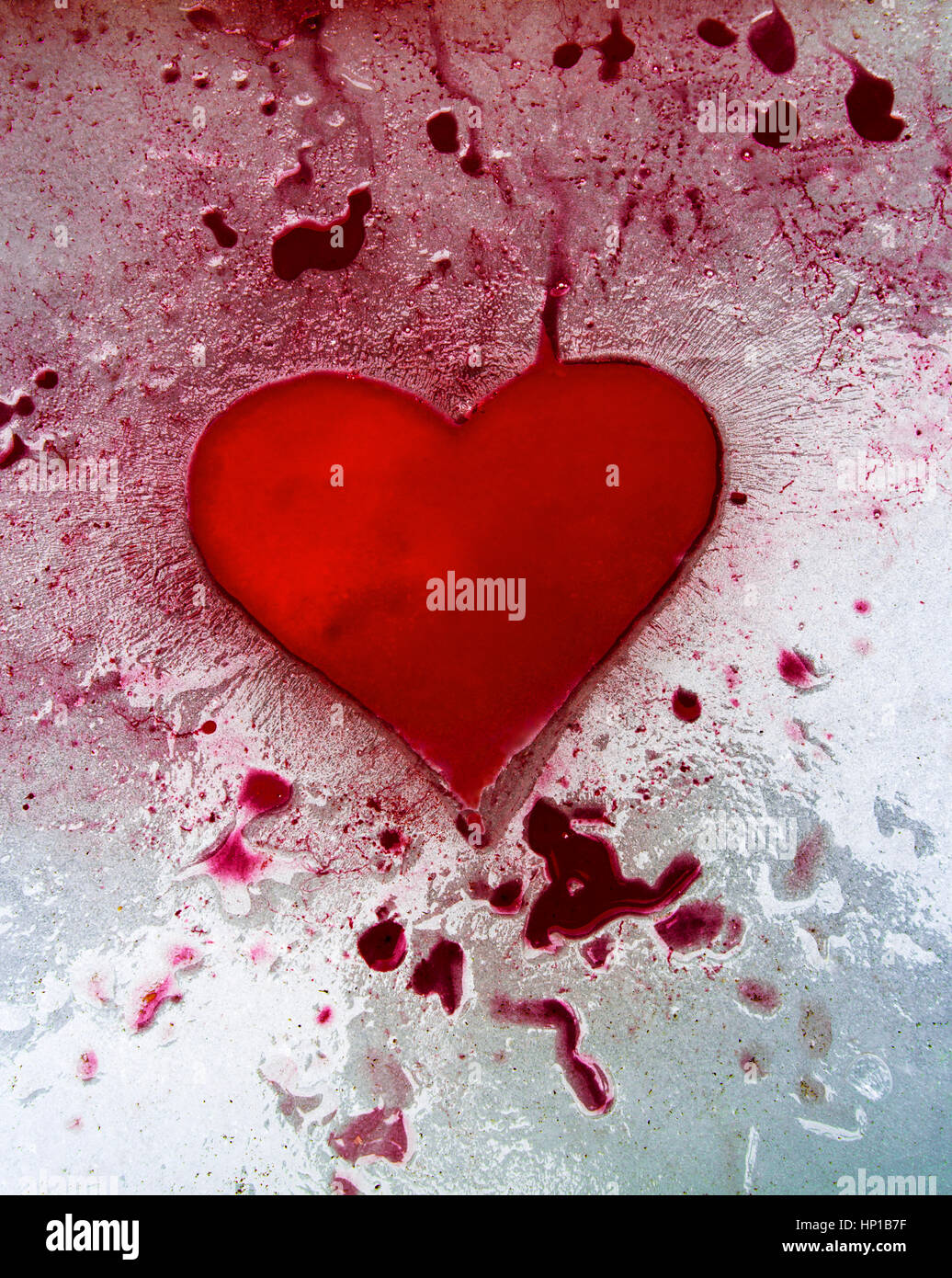 Red ink heart on ice. Red ink pooling into a heart shaped hollow, and across and into other depressions in the surface of ice. Stock Photo