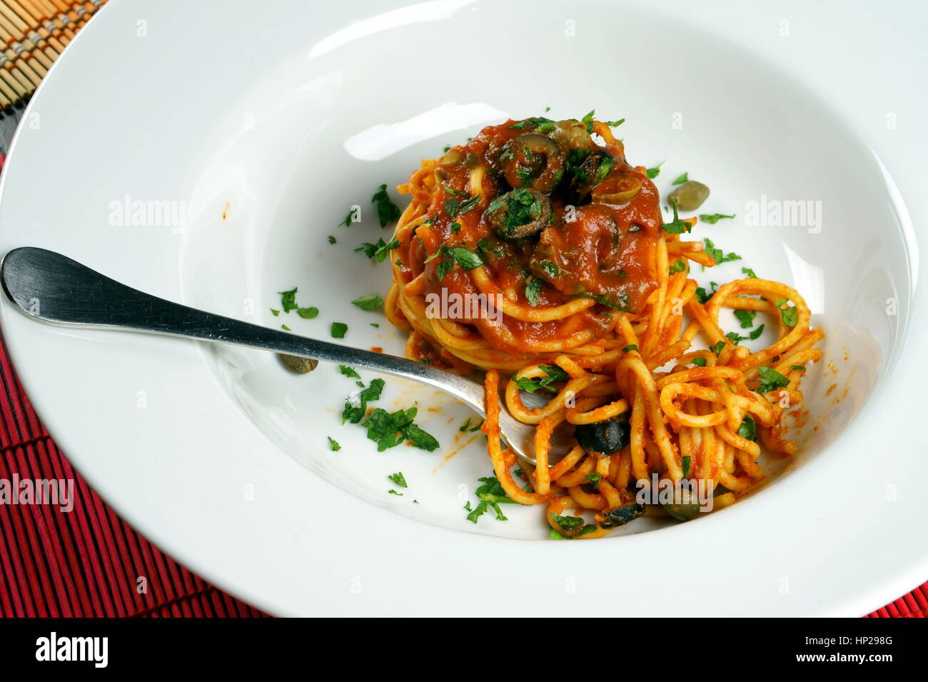 Spaghetti puttanesca with fork served in a white dish Italian recipe