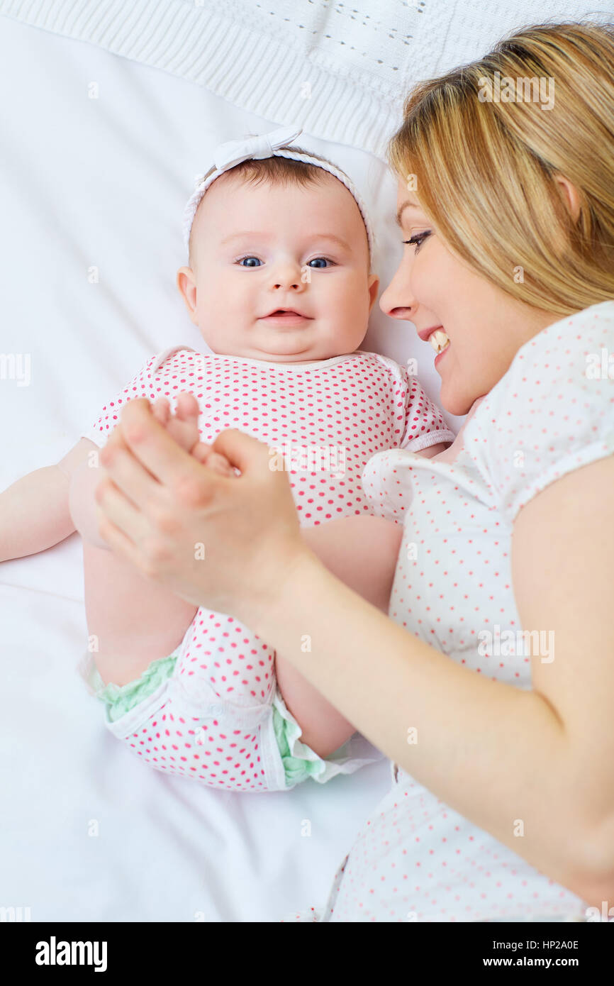Mother playing with her baby on the bed. Mom smiles to her child Stock Photo