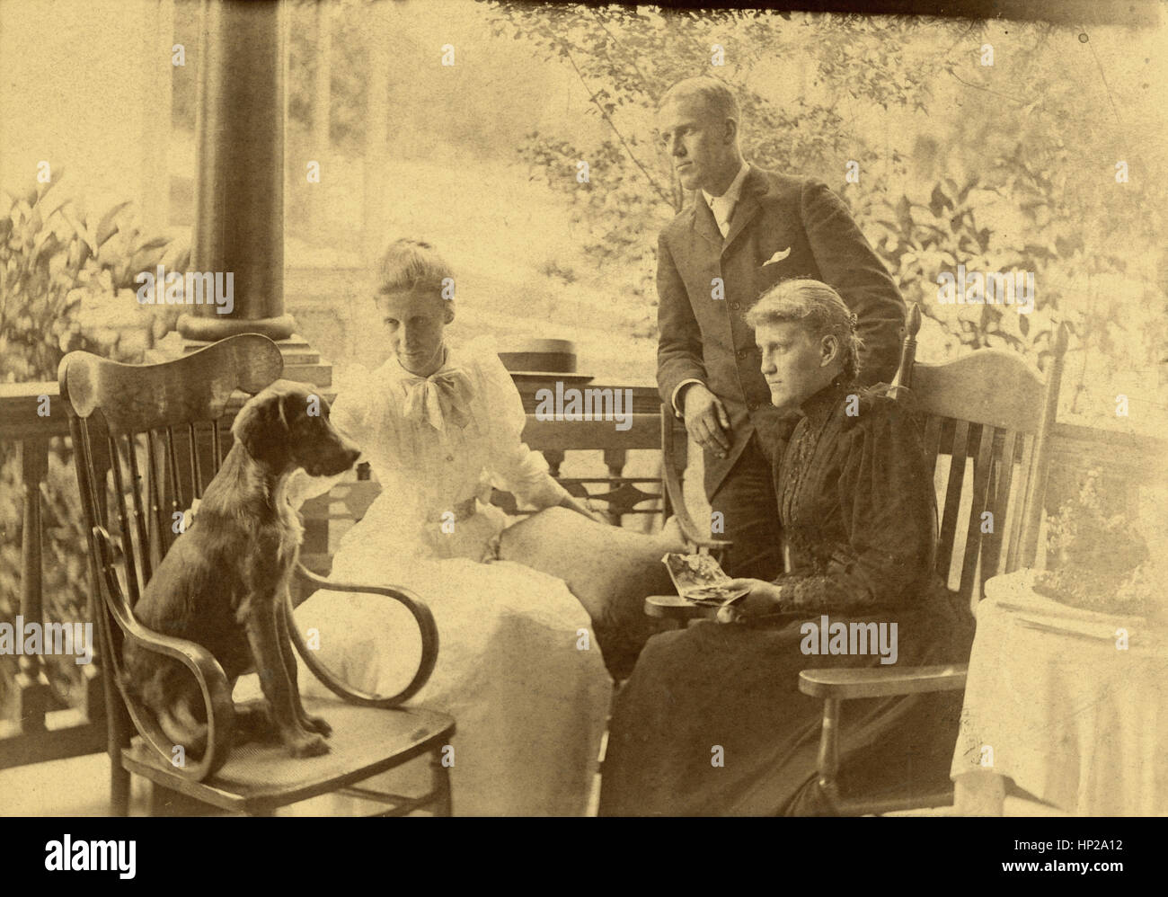 Antique c1890 photograph, group of Victorian adults on porch with dog. Location: New England, USA. SOURCE: ORIGINAL PHOTOGRAPHIC PRINT. Stock Photo