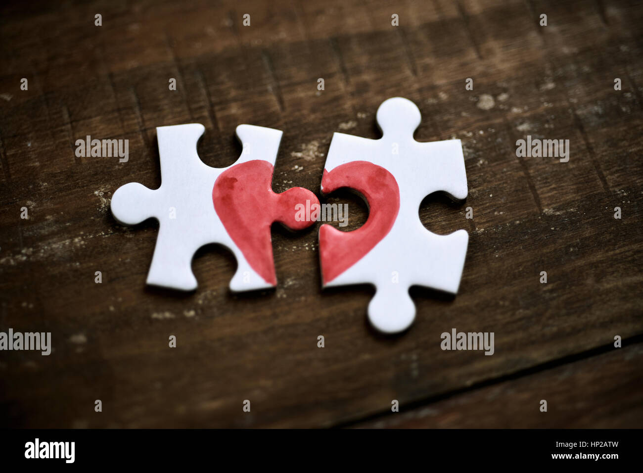 closeup of two separated pieces of a puzzle which together form a heart on a rustic wooden surface, depicting the idea of rupture or cooperation Stock Photo