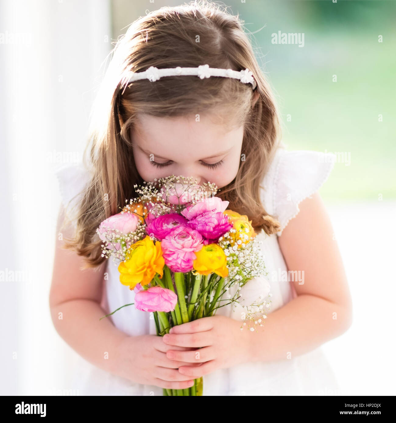 Cute little girl in white dress holding ranunculus flowers bouquet on ...