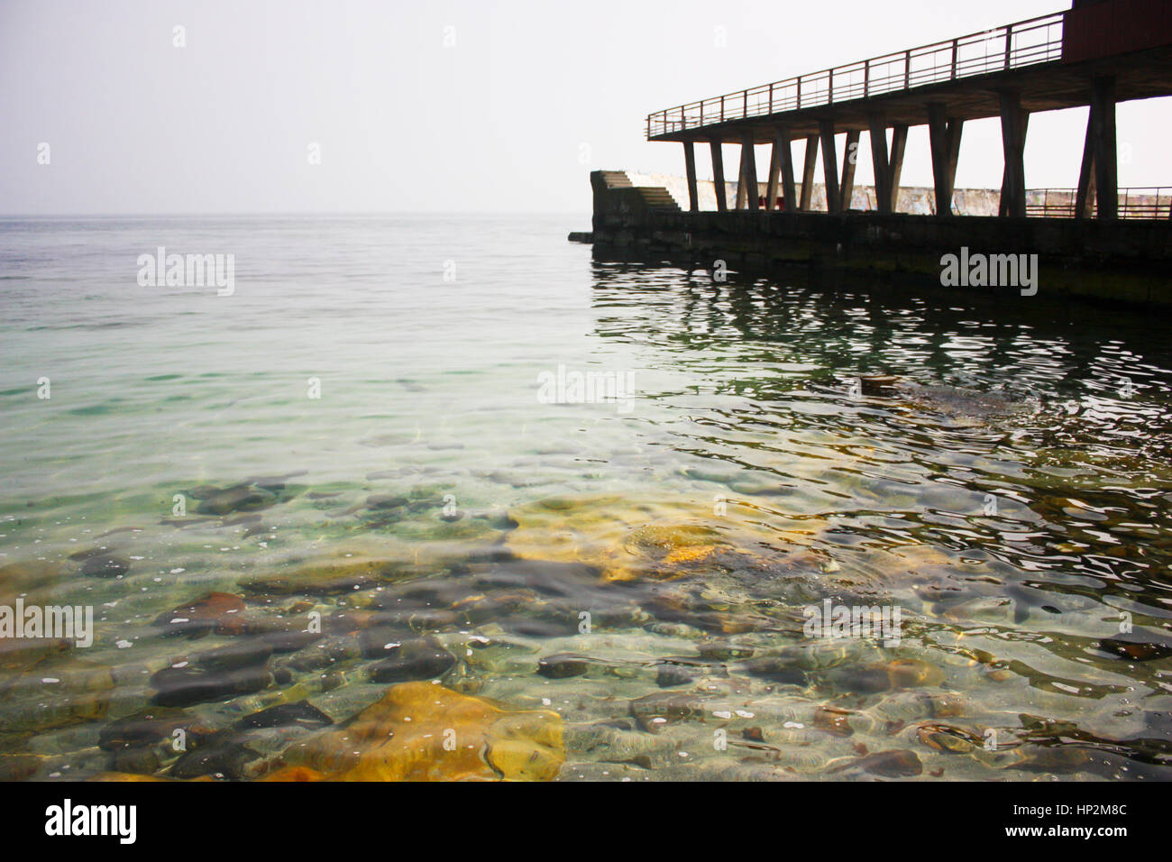 Old concrete, stone pier and the bridge in the sea. Beautiful dark sea with rich color and clear water and stones Stock Photo