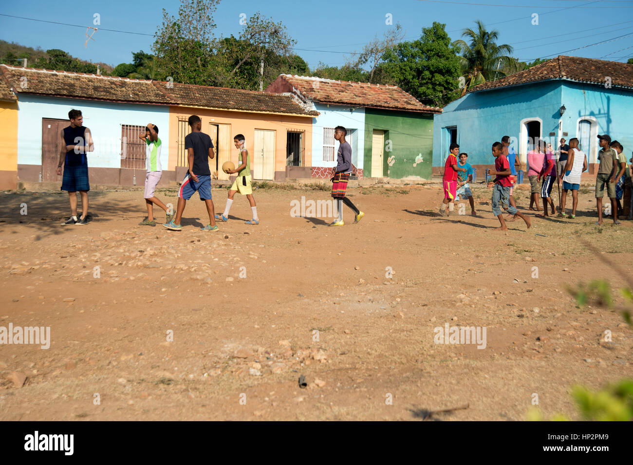 A group of young Cuban boys playing football on a rough ground football pitch in Trinidad Cuba with traditional Trinidad poor housing behind Stock Photo