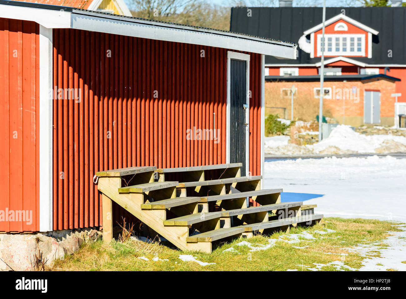 Makeshift wooden spectator bench or quire scene outside a red wooden shed. Thawing snow on the ground. House in background. Stock Photo