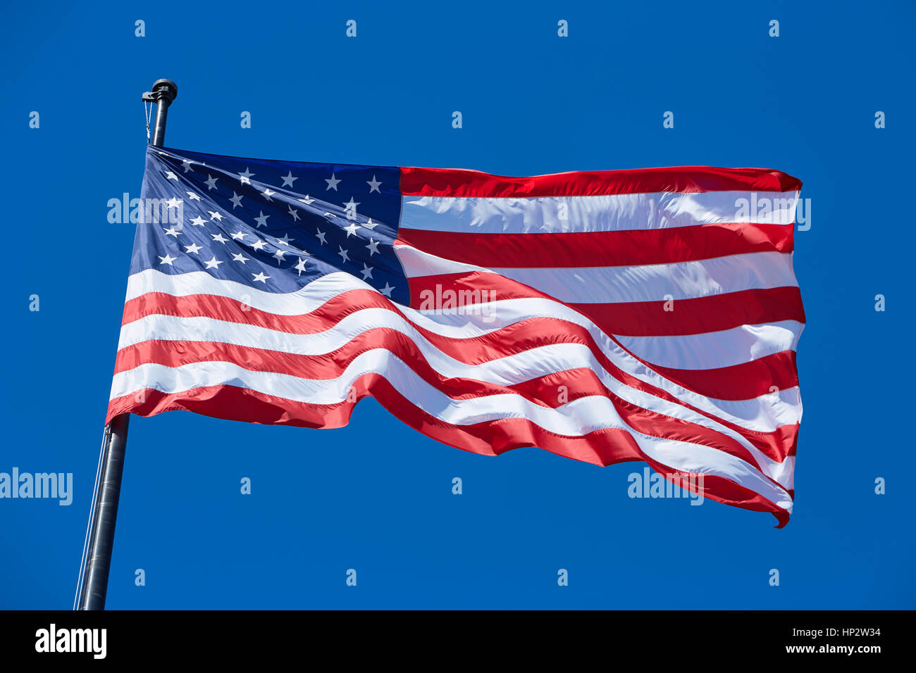 American or USA flag in wind with flagpole on clear blue sky Stock Photo