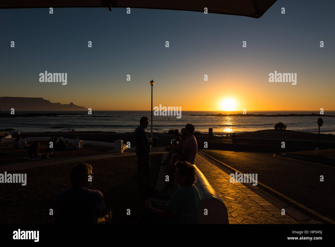 Cape Town, South Africa - November 15, 2016: Unidentified people are enjoying their drinks during the colorful sunset on the beach at Bloubergstrand i Stock Photo