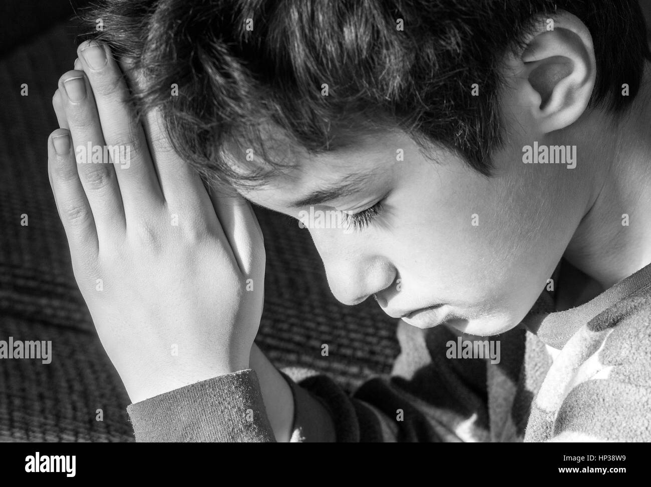 Young boy bowing his head and praying solemnly, black and white ...