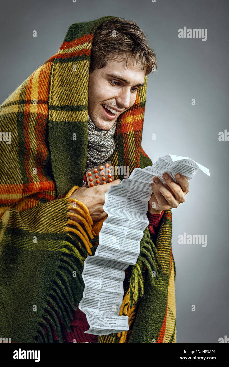 Happy sick man covered in blanket reads to instructions. Photo of man suffering cold and flu virus. Health care concept Stock Photo