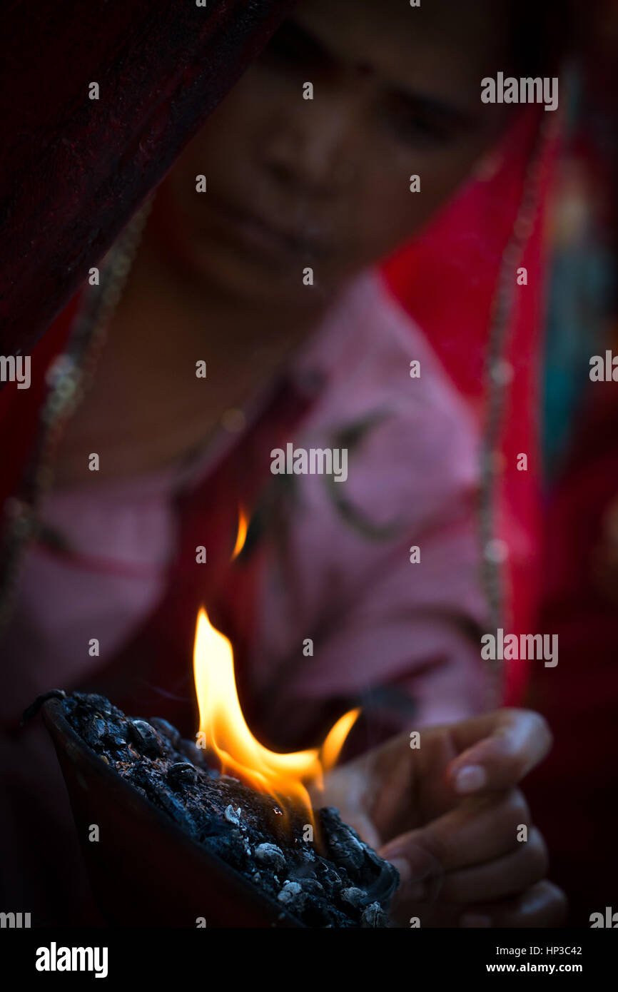 An Indian woman, wearing traditional red and pink clothes, touching the holy fire Stock Photo