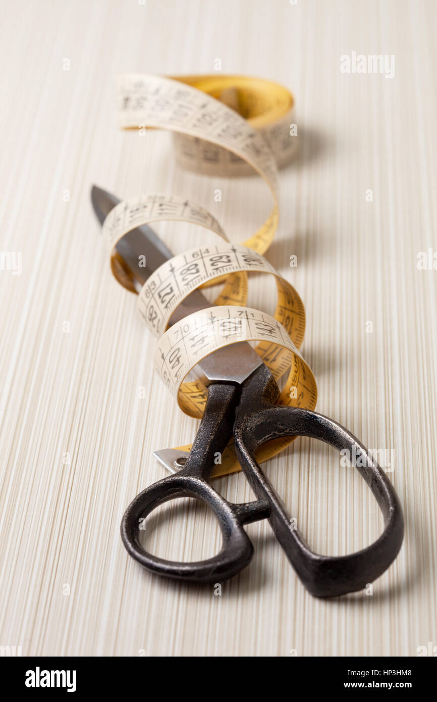 Sewing accessories and tools. Red sewing threads, black scissors, yellow  measuring tape and thimble on a white background. Stock Photo