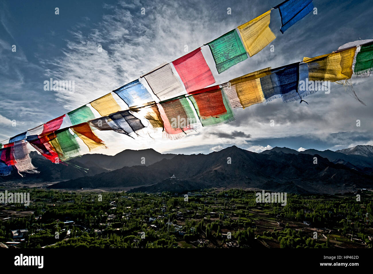 Buddhist prayer flags in foreground, shanti stupa, mountain range, greenery, clouds and the sky in background at Leh, Ladakh, India Stock Photo