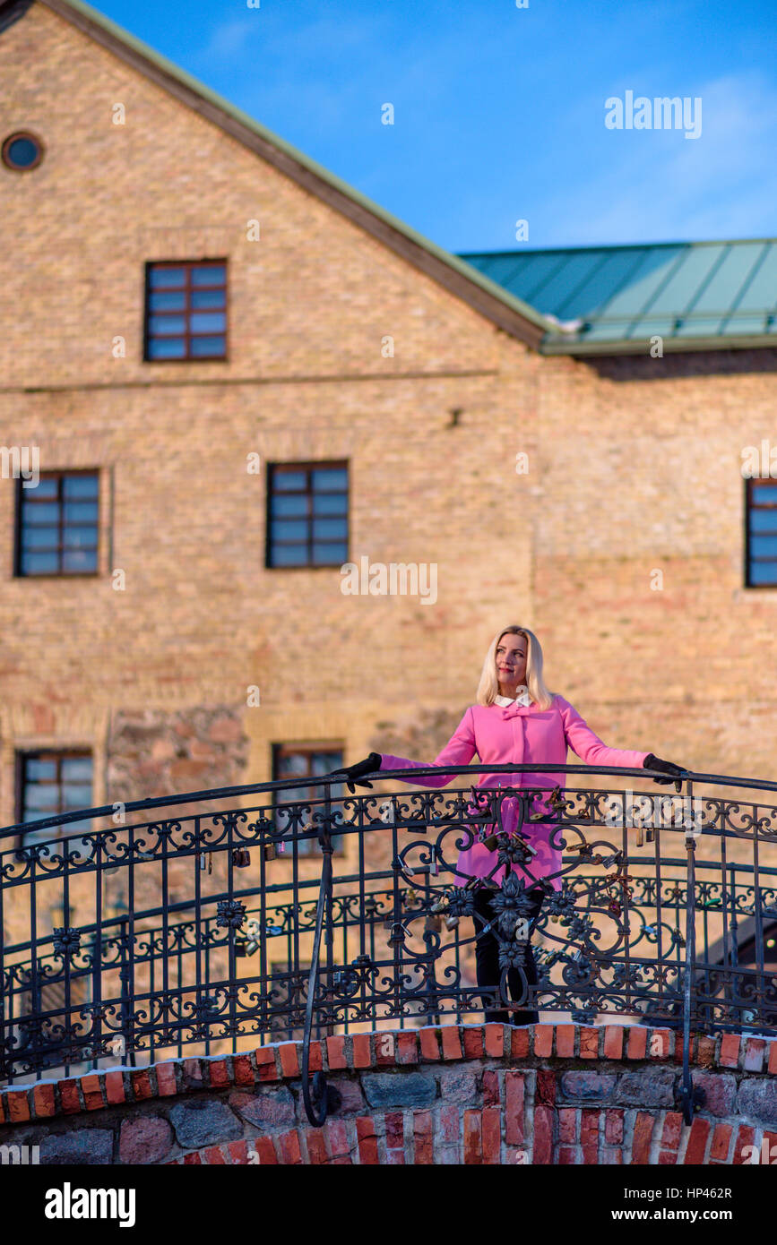 Beautiful female in pink coat leaning on the steel railing Stock Photo