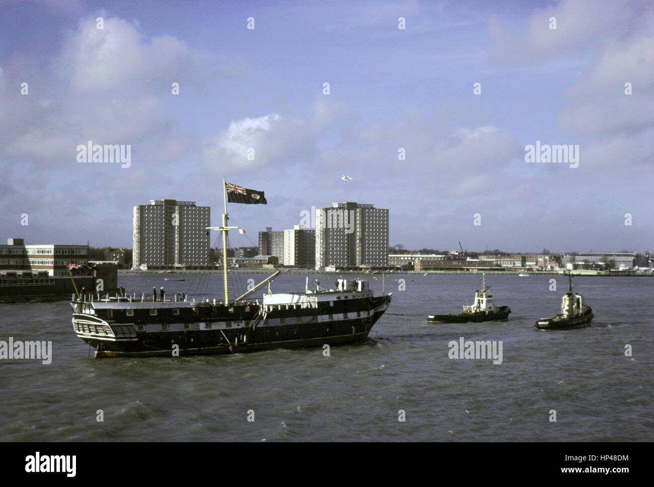 AJAXNETPHOTO. 21ST JANUARY, 1977. PORTSMOUTH, ENGLAND. - WOODEN WALL RETURNS -  T.S. FOUDROYANT (EX TRINCOMALEE) UNDER TOW ENTERING HARBOUR AFTER RECENT REFIT.  PHOTO:JONATHAN EASTLAND/AJAX  REF:2772101 4777 Stock Photo