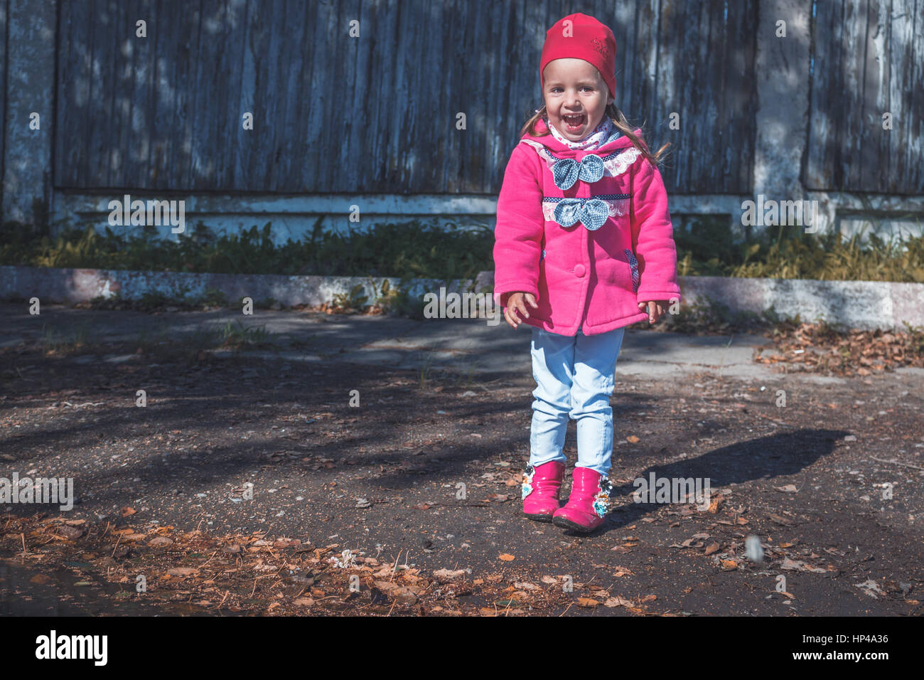 Little girl in a pink coat, jeans and pink boots walking in the park ...